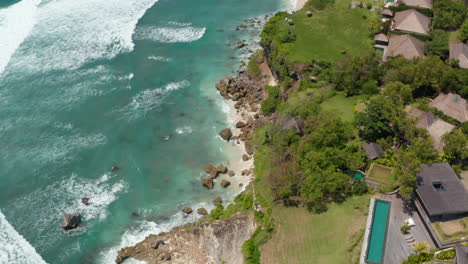 Overhead-aerial-view-of-luxury-tropical-villas-on-the-cliff-above-blue-ocean-and-sand-beaches-in-Bali,-Indonesia
