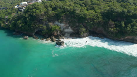 Wild-ocean-waves-crashing-on-rocky-cliff-in-tropical-Bali-coastline.-Aerial-view-of-turquoise-blue-water-splashing-around-the-rocky-cliffs