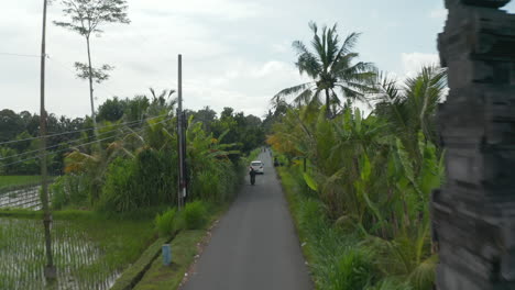 Cars-and-motorcycles-driving-on-rural-asphalt-streets-along-rice-fields-in-Bali,-Indonesia.-Aerial-view-of-traffic-on-rural-roads-through-farmland-and-rice-plantations-in-Asia