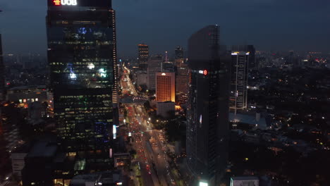 Aerial-dolly-shot-flying-towards-skyscrapers-above-busy-night-traffic-on-the-highway-in-Jakarta,-Indonesia