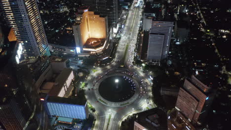 Aerial-night-drone-view-closing-in-on-Selamat-Datang-Monument-roundabout-with-fast-car-traffic-in-Jakarta,-Indonesia