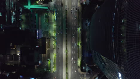Aerial-Birds-Eye-Overhead-Top-Down-View-of-city-traffic-at-night-next-to-skyscraper-tower-building-and-city-lights-flashing-in-Jakarta,-Indonesia