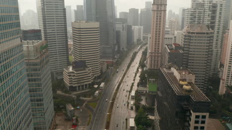 Rising-aerial-shot-tilting-into-overhead-view-of-car-traffic-on-a-multi-lane-highway-surrounded-by-tall-skyscrapers-in-Jakarta,-Indonesia