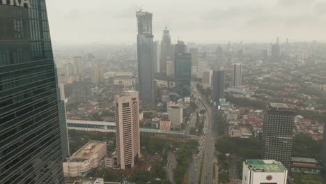 Aerial-view-reveal-flying-from-behind-a-skyscraper-to-wide-view-of-Jakarta-city-skyline-reveal-in-cloudy-weather