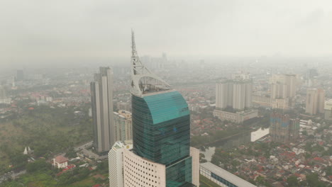Close-up-aerial-dolly-shot-of-the-top-of-Wisma-46-skyscraper-in-Jakarta,-Indonesia-on-a-cloudy-day