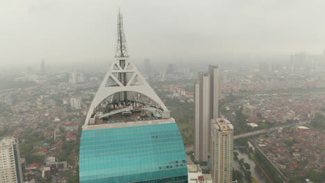 Close-up-circling-aerial-view-of-the-antenna-of-Wisma-46-skyscraper-in-Jakarta,-Indonesia-on-a-cloudy-day