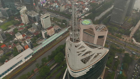 Aerial-pedestal-tilting-into-overhead-view-of-the-top-of-the-Wisma-46-skyscraper-in-Jakarta,-Indonesia-on-a-cloudy-day