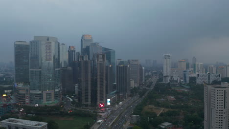Wide-aerial-dolly-shot-of-multiple-tall-glass-skyscrapers-and-wide-multi-lane-highway-in-modern-city-center-of-Jakarta