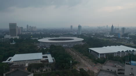 Wide-aerial-dolly-shot-of-modern-athletic-Gelora-Bung-Karno-stadium-in-urban-city-center-and-city-skyline-in-the-background-in-Jakarta