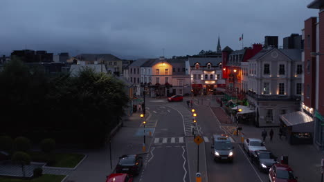 Forwards-fly-above-road-and-roundabout-in-town.-Illuminated-colourful-house-facades-along-streets-at-dusk.-Killarney,-Ireland-in-2021