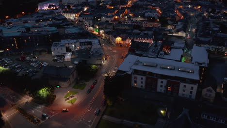 Aerial-descending-footage-of-night-city.-Illuminated-streets-and-house-facades-in-town-centre.-Killarney,-Ireland