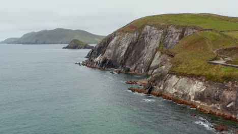 Fly-along-sea-coast.-High-and-steep-rock-slope-rising-from-water-with-green-grass-on-top.-Beautiful-natural-scenery.-Ireland