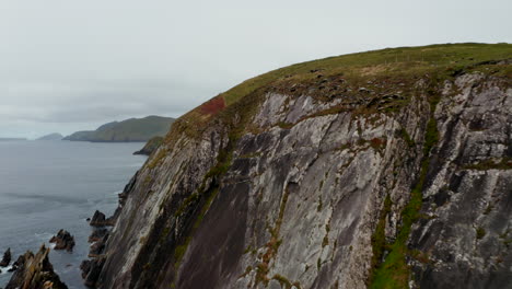 Forwards-fly-around-steep-rock-cliff-and-green-grass-top-of-Dunmore-Head-promontory.-Revealing-islands-in-sea.-Ireland
