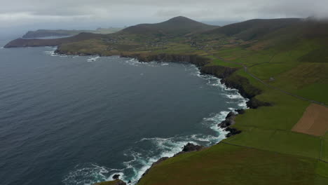 Aerial-panoramic-shot-coastal-landscape.-Waves-crashing-on-rocky-coast-and-making-white-foam.-Green-pastures-and-villages-in-countryside.-Ireland