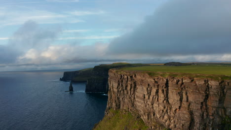 Beautiful-footage-of-sea-coast-with-high-rocky-cliffs-at-sunset.-Fly-around-tip-of-rock-edge.-Cliffs-of-Moher,-Ireland