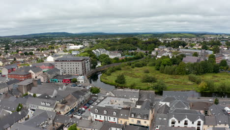 Slide-and-pan-aerial-shot-of-buildings-in-town.-River-Fergus-calmly-flowing-along-houses.-Ennis,-Ireland