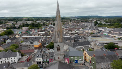 Fly-around-tall-spire-of-Catholic-cathedral.-Aerial-view-of-town-development.-Buildings-and-streets-in-town-centre.-Ennis,-Ireland
