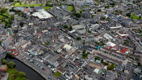 Forwards-fly-above-town.-High-angle-view-of-centre-with-buildings-and-squares.-Tilt-down-focusing-on-roundabout-with--sculpture-in-middle.-Ennis,-Ireland