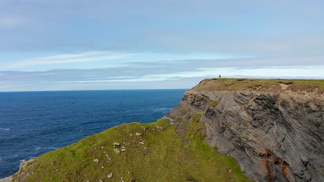 Forwards-fly-above-sea-coast.-High-rocky-cliffs-steeply-falling-to-sea.-Revealing-waves-crashing-to-coast.-Kilkee-Cliff-Walk,-Ireland