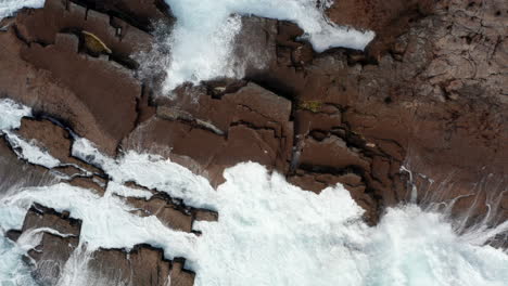 Aerial-birds-eye-overhead-top-down-view-of-waves-rolling-over-rock-platform-and-splashing-into-height.-Detailed-footage-of-power-of-nature.-Kilkee-Cliff-Walk,-Ireland