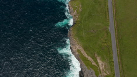 Aerial-birds-eye-overhead-top-down-view-of-waves-rolling-to-coast-and-crashing-on-cliffs.-Fly-above-sea-coast.-Kilkee-Cliff-Walk,-Ireland