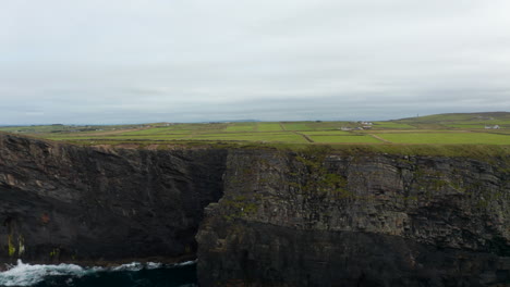 Slide-and-pan-footage-of-tourists-standing-on-edge-of-cliff-high-above-water.-Vertical-rock-wall-on-sea-coast.-Kilkee-Cliff-Walk,-Ireland