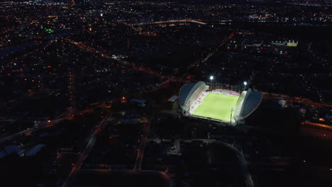 Amazing-aerial-shot-of-bright-football-arena-contrasting-with-night-city.-Bright-light-shining-on-green-football-playfield.-Limerick,-Ireland