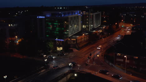Elevated-shot-of-cars-passing-through-crossroads-in-night-city.-Colour-illuminated-building-on-corner.-Limerick,-Ireland