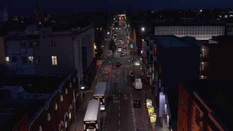 Forwards-tracking-of-group-of-cars-driving-in-one-way-street-in-night-city.--Road-lined-by-parked-vehicles-and-townhouses.-Limerick,-Ireland