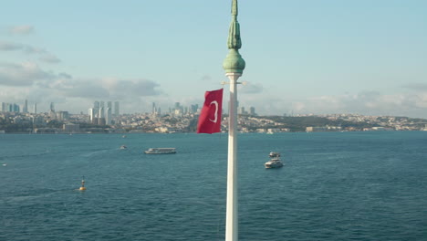 Vibrante-Bandera-Roja-Turca-Ondeando-En-El-Viento-En-La-Parte-Superior-De-La-Torre-De-La-Doncella-En-El-Agua-En-Estambul,-Toma-Aérea-En-Círculos