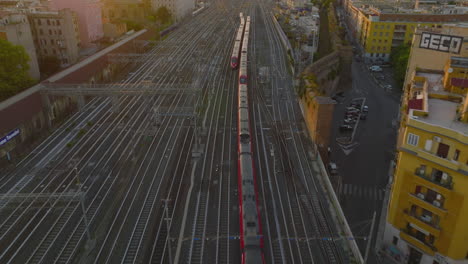 High-angle-view-of-two-modern-train-units-passing-by-each-other-on-wide-multitrack-railway.-Tilt-up-reveal-Roma-Termini-train-station-at-golden-hour.-Rome,-Italy