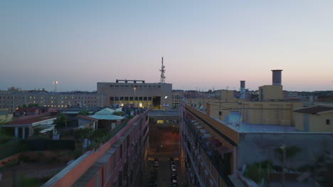 Forwards-fly-above-street-and-buildings-in-urban-borough-at-dusk.-Revealing-railway-tracks-near-train-station.-Rome,-Italy