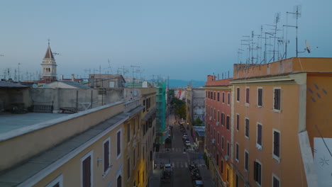 Rooftop-sliding-reveal-of-street-between-apartment-buildings-in-urban-borough.-City-at-twilight.-Rome,-Italy