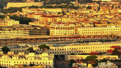 Zoomed-shot-of-city-at-sunrise.-Tracking-of-commuter-train-unit-approaching-train-station.-Rome,-Italy