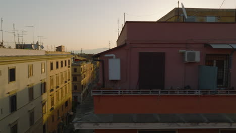 Colour-facade-with-windows-and-balcony-on-top-floor-of-residential-building.-Sliding-reveal-of-street-in-city-at-sunrise.-Rome,-Italy