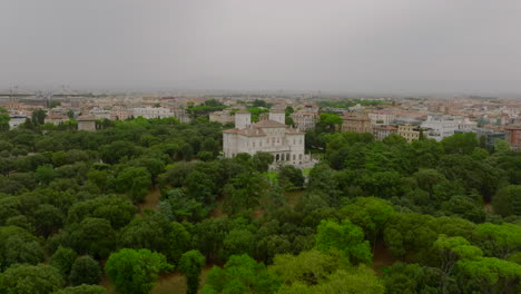 Beautiful-historic-building-among-green-trees-in-park-and-buildings-in-city-on-cloudy-day-in-background.-Borghese-Gallery.-Rome,-Italy