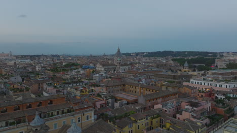 Forwards-fly-above-city-at-twilight,-heading-towards-San-Carlo-al-Corso,-basilica-with-large-dome.-Rome,-Italy