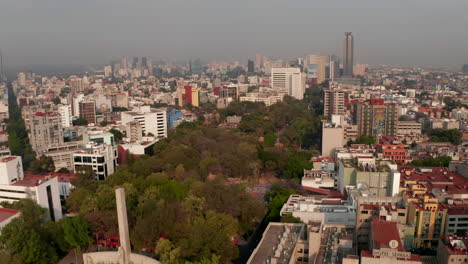 Aerial-view-from-drone-flying-over-town-park-surrounded-by-urban-housing.-Camera-tilting-up-to-wide-cityscape.-Mexico-city,-Mexico.