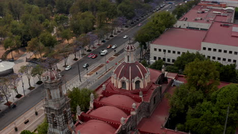 Elevated-view-of-church-with-red-dome-and-public-town-park-Alameda-Central.-Drone-camera-flying-over-building-in-downtown.-Mexico-city,-Mexico.