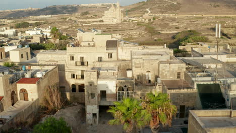 Houses-with-Solar-Panel-and-Roof-Terrace-in-Mediterranean-Country-Malta-in-Brown-and-Beige-Sand-Color-with-View-over-Countryside-and-Church,-Aerial-forward-Dolly