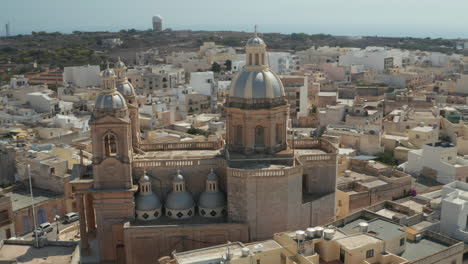 Beautiful-Blue-and-Brown-Church-Towers-in-Small-mediterranean-Town-on-Malta-Island,-Aerial-Slide-Right-in-Sunset-light