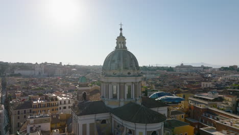 Orbit-shot-around-church-tower-with-large-dome.-San-Carlo-al-Corso-and-buildings-in-city-in-background.-Rome,-Italy