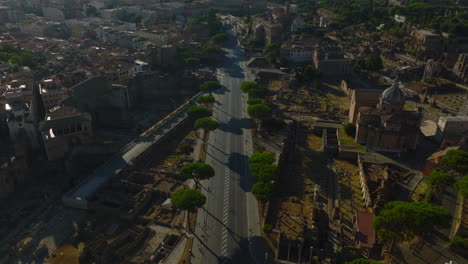 High-angle-view-of-road-in-city-surrounded-by-remains-of-ancient-sites.-Tilt-up-reveal-of-cityscape-with-Colosseum-amphitheatre-in-distance.-Rome,-Italy