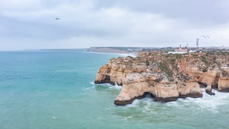 Aerial-drone-hyper-lapse-circling-around-beautiful-Lagos-Algarve-coastline-with-waves-crashing-against-rocky-cliffs,-cloudy-day