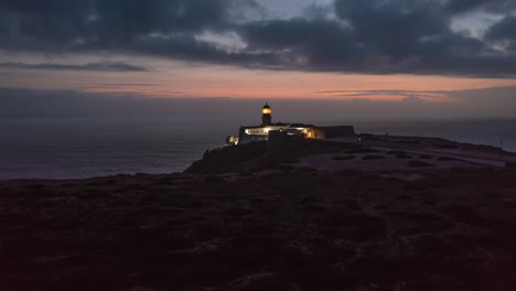 Aerial-drone-hyper-lapse-of-flashing-lighthouse-at-dusk.-Ponta-da-Piedade-Lighthouse-in-Lagos-Algarve,-Portugal,-drone-flying-forward-towards-head-lamp,-evening