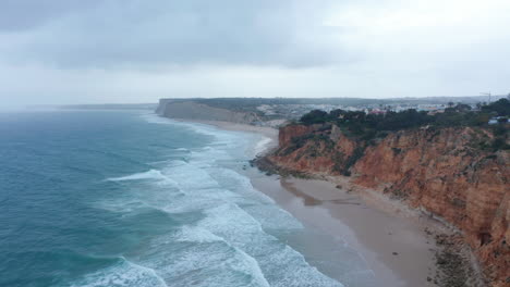 Amazing-aerial-drone-view-of-sandy-Lagos-beach-with-waves-crashing-against-shore,-cloudy-day,-dolly-in
