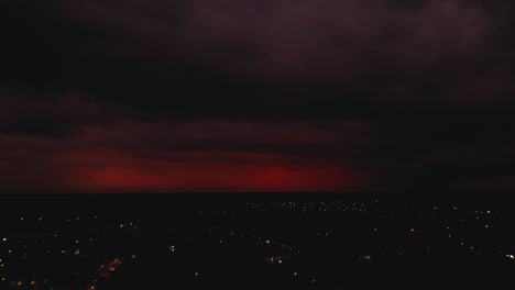 Fly-above-night-city.-Red-clouds-and-seldom-flash-of-lightning.-Storm-in-distance.-Valladolid,-Mexico