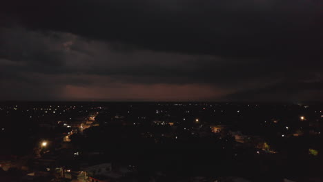 Aerial-panoramic-footage-of-modestly-illuminated-streets-in-night-town.-Heavy-clouds-and-storm-with-lightning-in-distance.-Valladolid,-Mexico