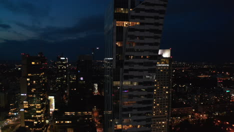 Rising-footage-of-modern-futuristic-office-or-apartment-tower-in-city-centre.-Night-view-of-downtown.-Warsaw,-Poland