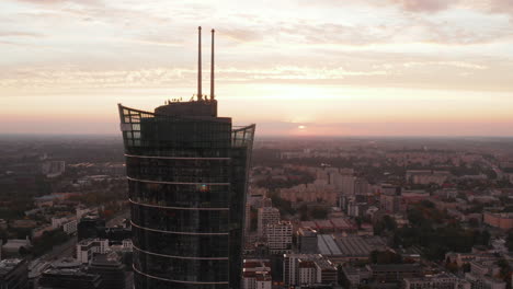 Orbit-shot-around-top-of-modern-futuristic-tall-building.-Warsaw-Spire-against-pink-twilight-sky.-Warsaw,-Poland